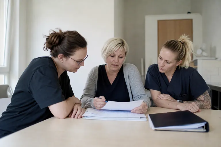 Team eines ambulanten Pflegedienstes bespricht Zuständigkeiten anhand von Unterlagen.